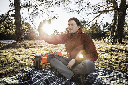 森林里坐在野餐毯上用手机自拍的年轻人图片