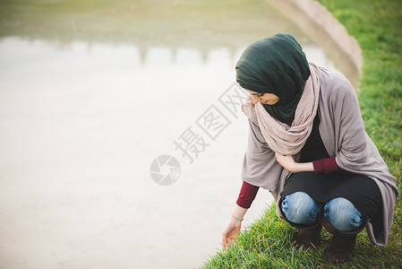身戴头巾的年轻女子在公园湖旁边蹲下图片