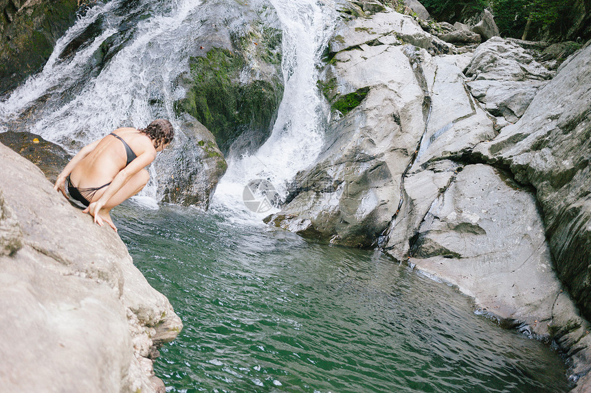 一个女人想跳进森林的游泳池带着瀑布图片