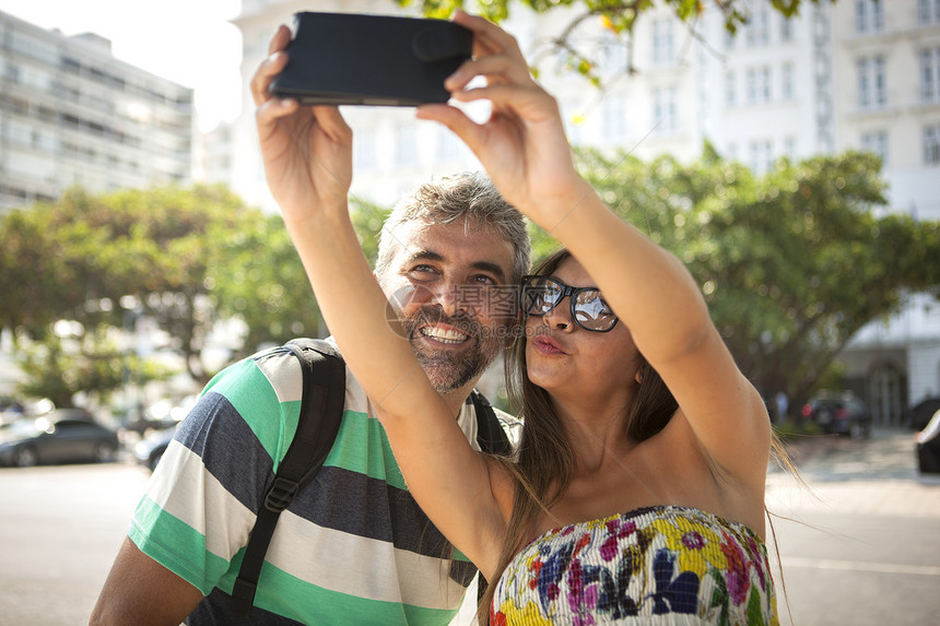 巴西里约热内卢科帕卡巴纳年轻女和成熟男在智能手机上自拍图片