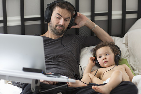 父亲和幼儿女在床上戴着耳机听音乐图片