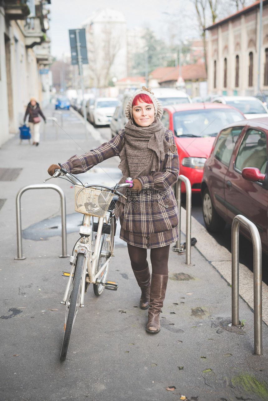 穿着冬季服装骑自行车在街上走的青年妇女图片