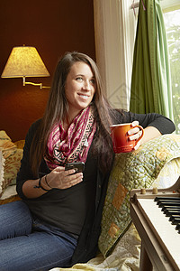 年轻女士喝着咖啡靠在沙发上仰望着窗外图片