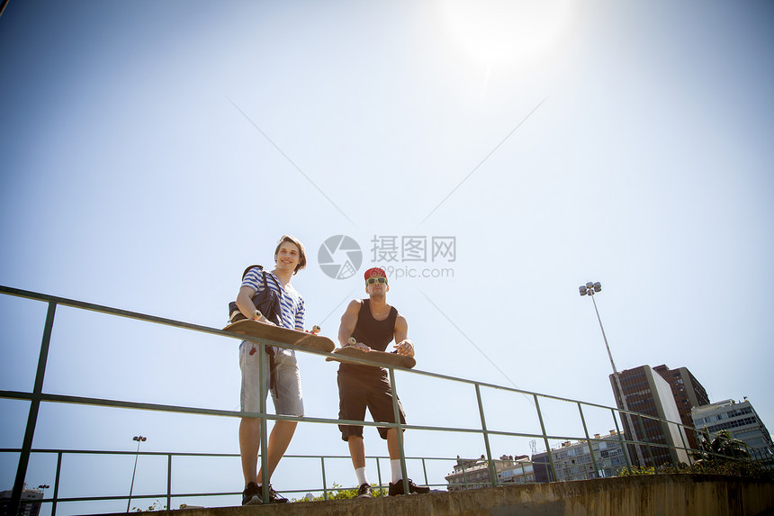 两个男人拿着滑板靠在栏杆上远望图片