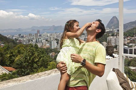 父亲在阳台上抱着捏父亲鼻子的女儿图片