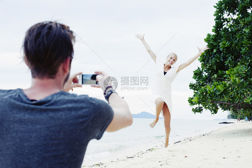 年轻男子拍摄女友在泰国克拉丹海滩上跳跃图片