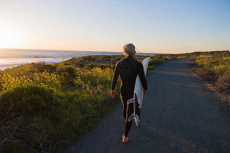 日出时的年轻男子在沿海农村公路上携带冲浪板高清图片