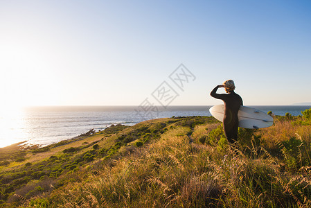 年轻男冲浪者从悬崖顶向大海眺望图片