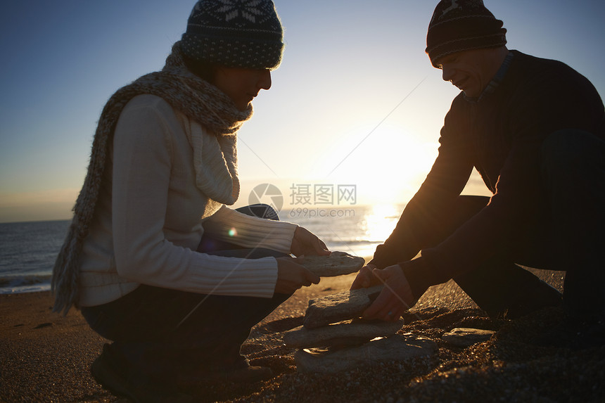 黄昏海滩上堆石头的夫妇图片