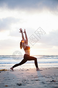 日落海滩上做瑜伽的年轻女性图片