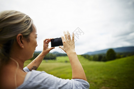 使用手机拍摄农村田地景观照片的女性图片