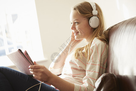 戴着耳机靠着沙发的女孩听数字平板电脑的音乐图片