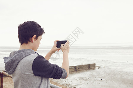 用智能手机拍摄大海照片的少年男孩图片