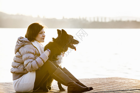 年轻女子和狗狗坐在码头上看日落图片