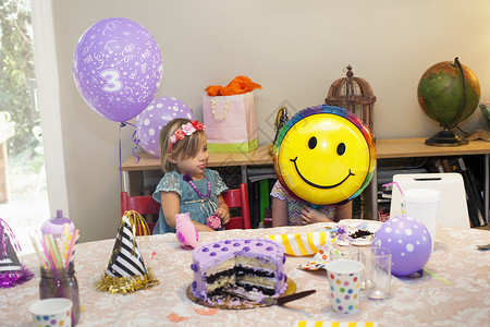 两个女孩坐在生日晚会桌边玩蛋糕笑脸气球背景图片