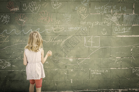 女孩站在墙前用粉笔写字图片