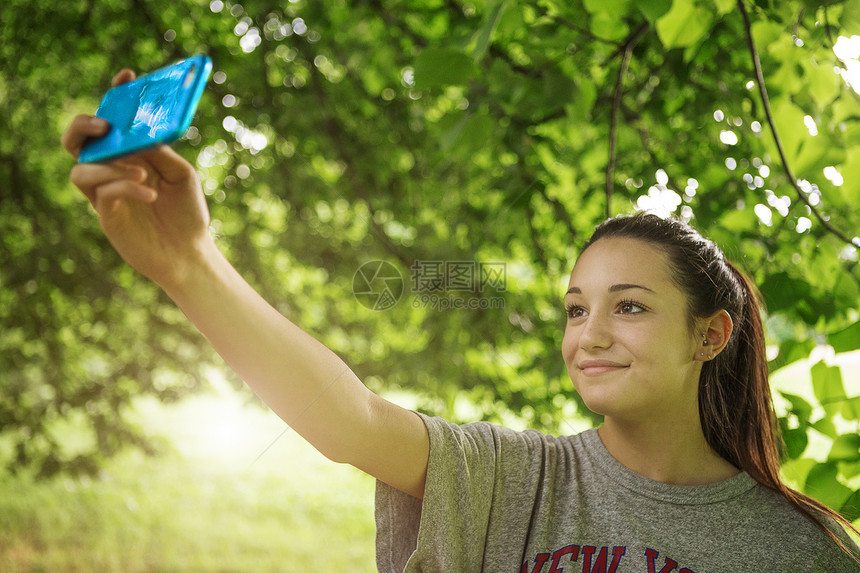 年轻女孩在公园使用智能手机自拍图片