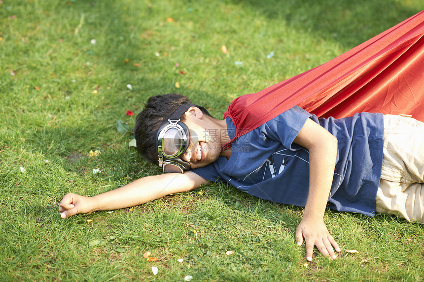 男孩身穿护目镜和斗篷坐在草地上立飞行姿势图片