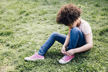 穿着粉色鞋的女孩坐在草地上系着鞋带往下看图片