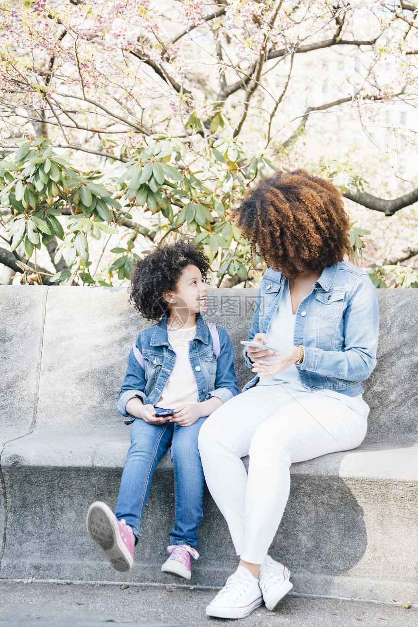 母亲和女儿并肩坐在一边拿着智能手机面对地图片