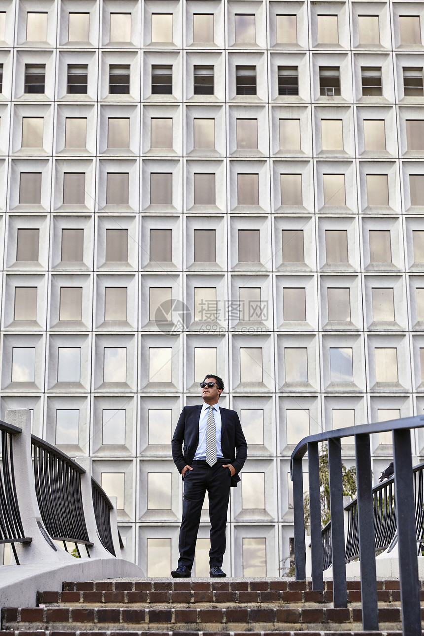 商人站在楼梯的顶端戴着太阳眼镜手放在口袋里向外看图片