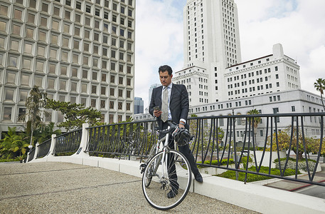 美国加利福尼亚州洛杉矶市政厅商人骑着自行车在高架人行道上看着智能手机图片