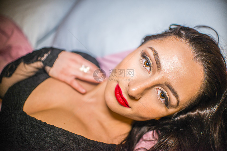 穿着红唇膏躺在床上的迷人年轻女子肖像图片