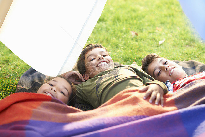 女孩和两个兄弟裹着毯子躺在花园里图片