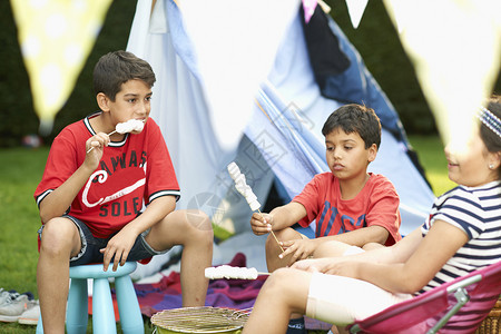 女孩和兄弟在花园内自制帐篷前吃烤棉花糖图片