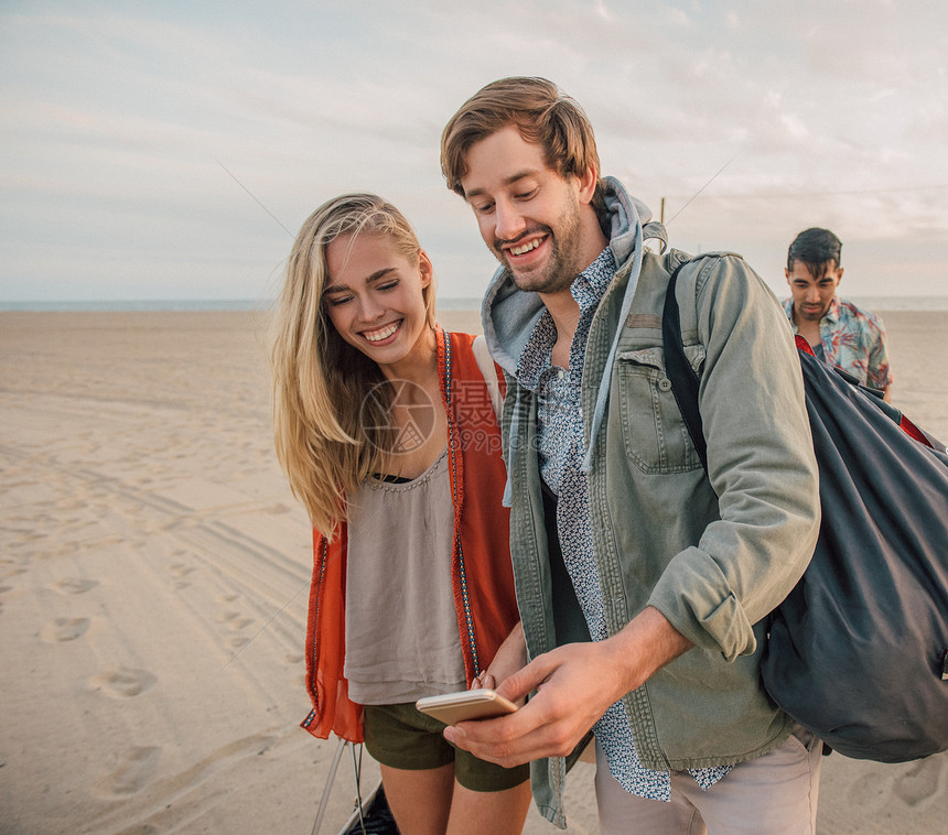 一群朋友在海滩上散步一对年轻夫妇看着智能手机图片