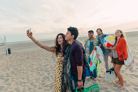 一群朋友在海滩上散步年轻夫妇用智能手机拍摄自画像图片