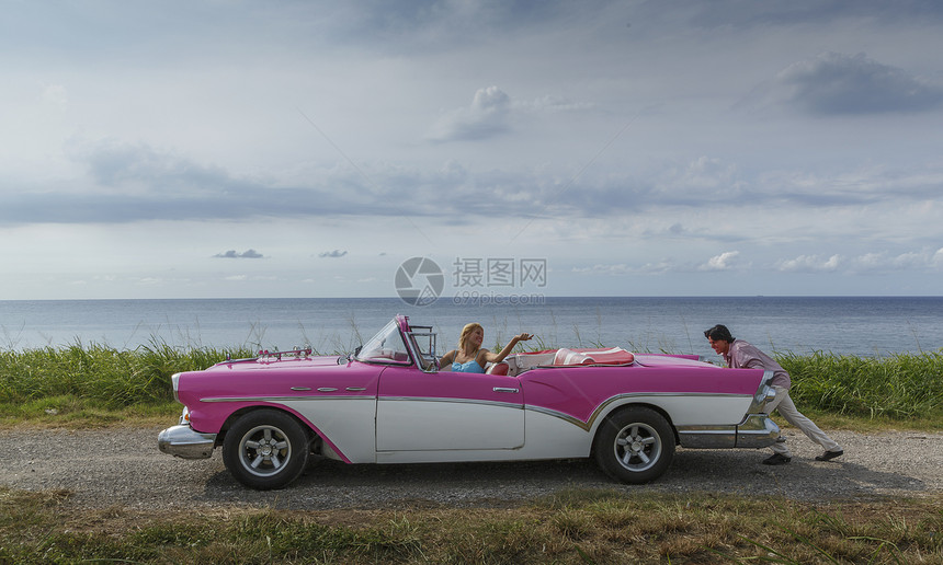 年轻男子在古巴哈瓦那的沿海推着老式敞篷车在女友驾时一边在古巴哈瓦那推着老式敞篷车图片
