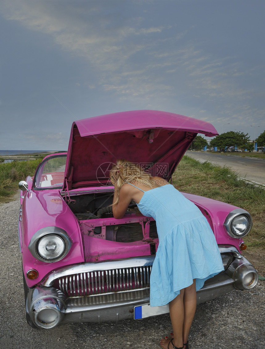 在古巴哈瓦那海岸试图修旧型敞篷车的年轻女子图片