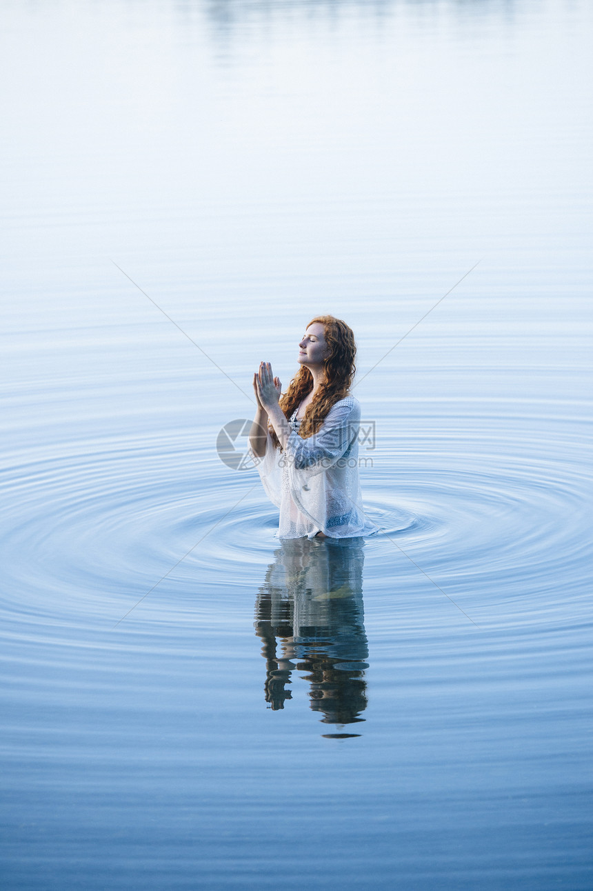 站在湖边的年轻女人闭着双眼手紧地站在湖边的波纹中图片