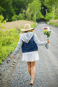 看见赤脚的年轻妇女走在农村砂砾路带着一束鲜花图片