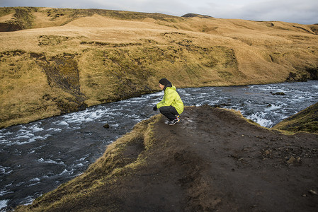 男游客蹲在冰岛斯科加福河岸边图片