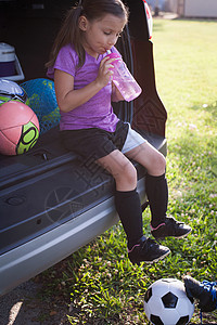 坐在汽车后备箱里喝水的女足球运动员图片