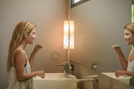 年轻妇女在刷牙时看着卫生间镜子图片