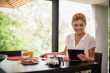 早餐桌上的年轻妇女浏览数字平板电脑图片