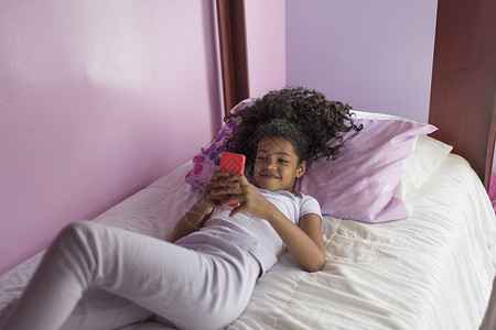 穿着睡衣躺在床上看智能手机的女孩高角度视角图片