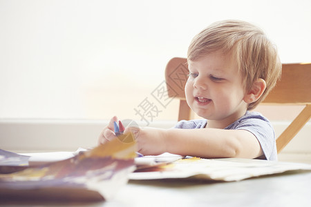 男孩坐在桌子上拿着蜡笔微笑地看着图片