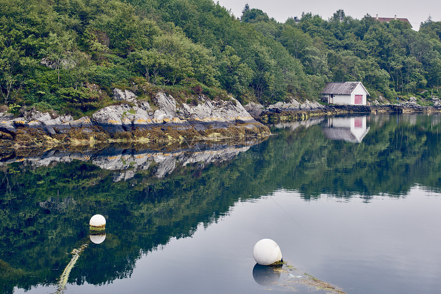 挪威罗加兰县豪格松平静水中的船库和树木倒影图片