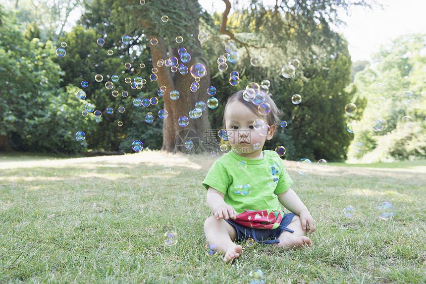坐在公园草地上看泡泡的男孩图片