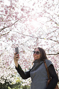 在樱花树下使用手机自拍的年轻女性图片