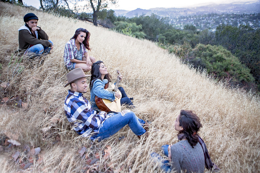 年轻女性在草地山上为朋友们弹吉他图片