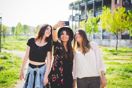 三名年轻女朋友在公园用智能手机自拍图片