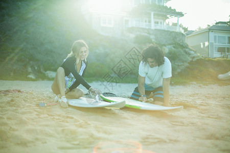 坐在沙滩上冲浪板打蜡的一对夫妇图片