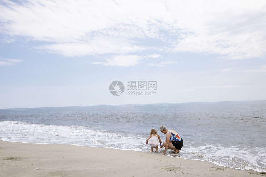 高级妇女和孙子在海上蹲和玩耍图片