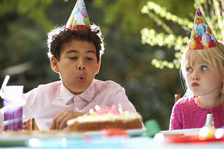 男孩吹生日蛋糕上的蜡烛在花园生日派对上图片