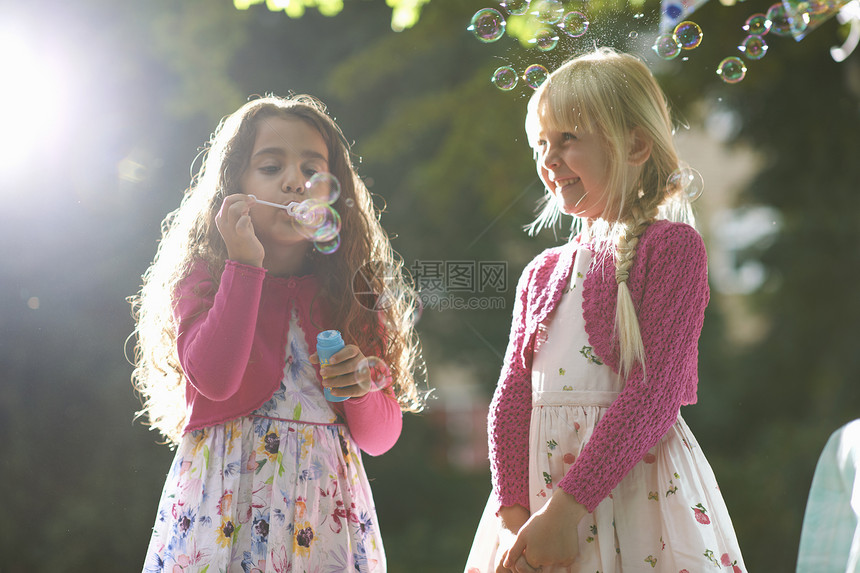 两个可爱的女孩在阳光花园吹泡泡图片